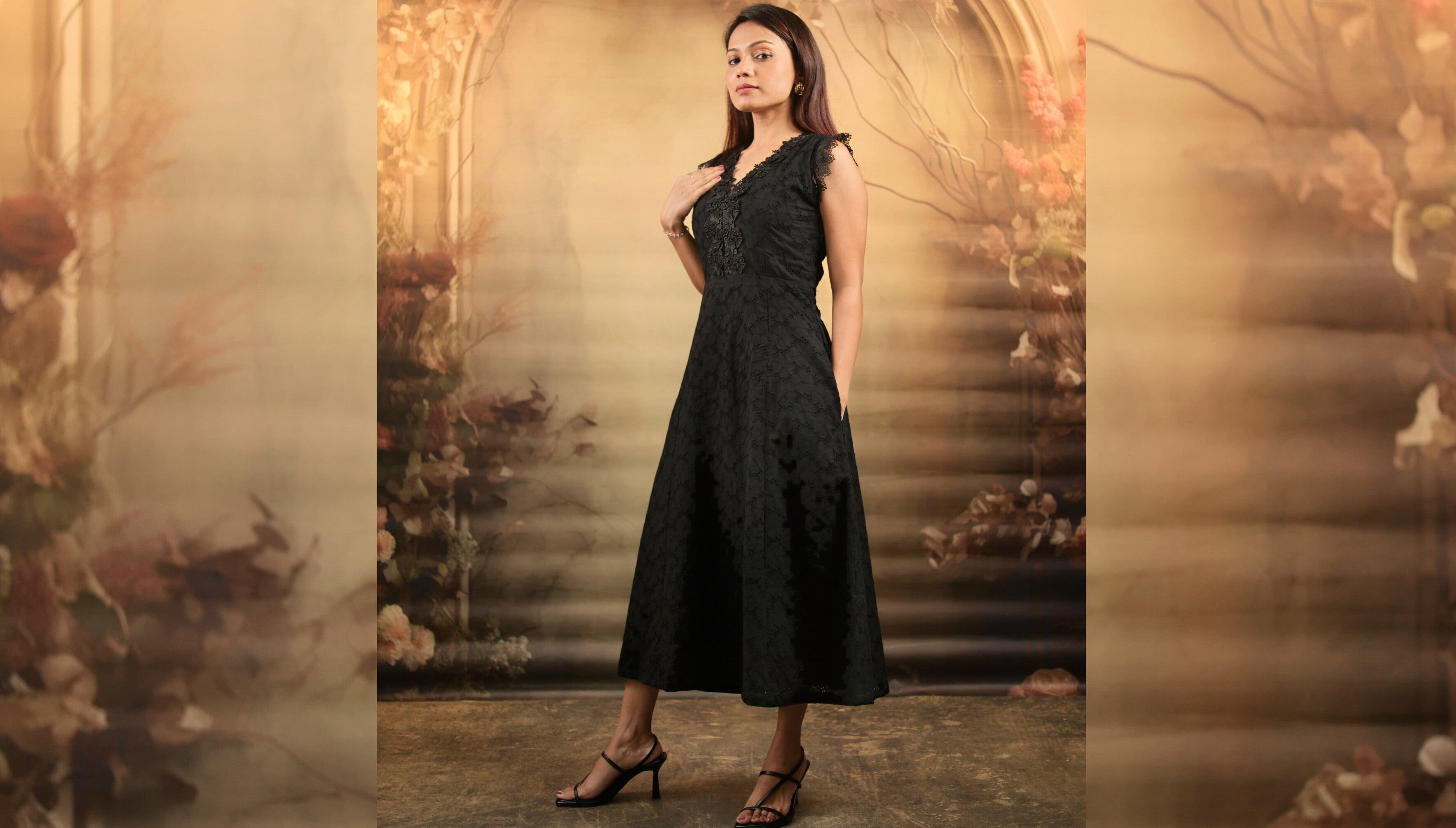 Petite Woman in a cotton lacey black dress standing in an ornate, dimly lit room with floral decorations.