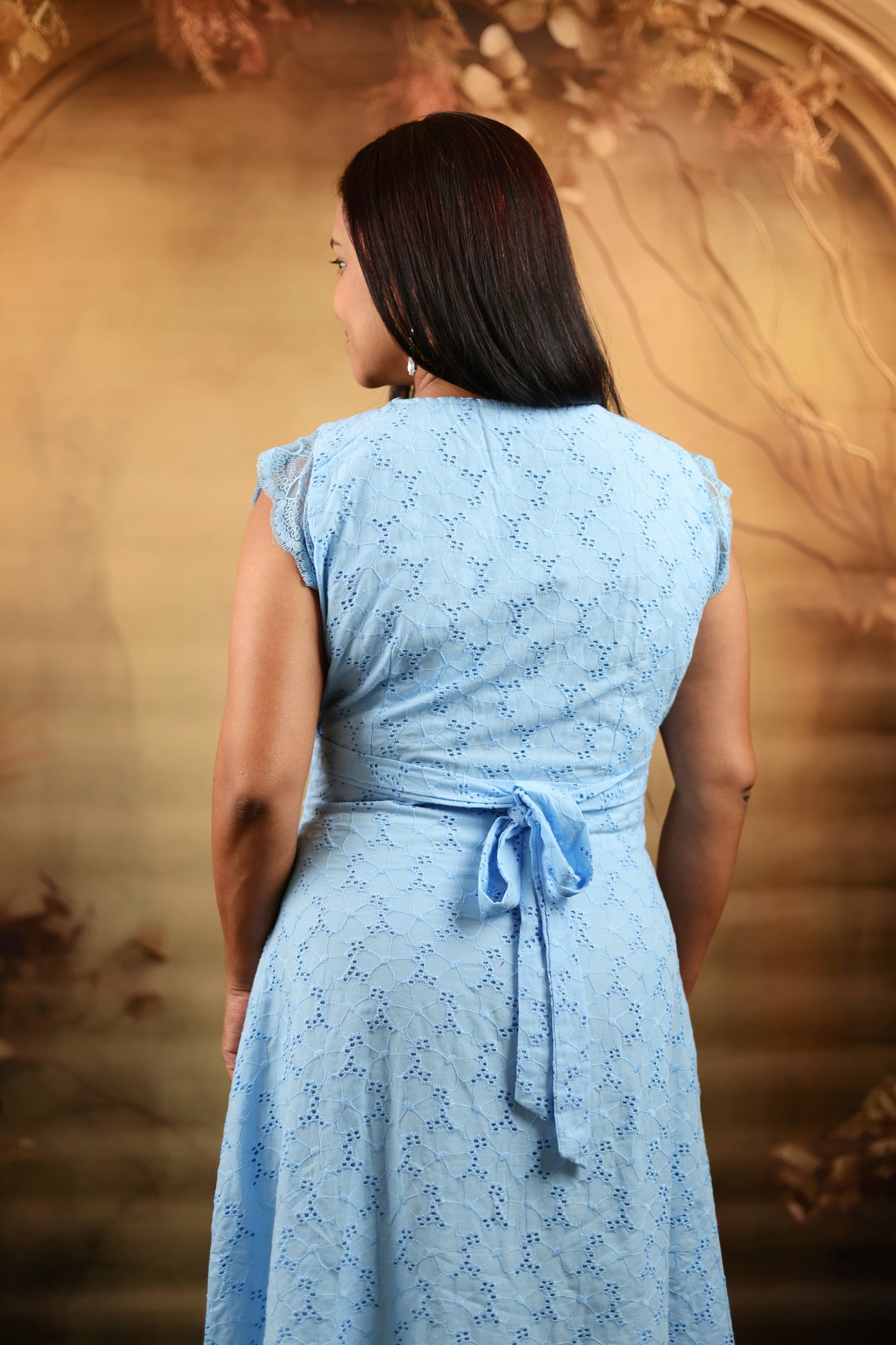 Woman wearing a light blue dress with a floral pattern against a decorative wall.