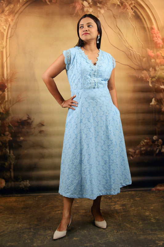 Woman wearing a light blue dress standing against a decorative background with flowers and branches.